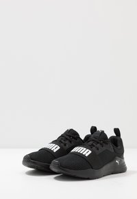 Zwarte sportieve schoenen met een bovenwerk van mesh, rubberen zool en een dikke witte logo aan de voorkant. Beschikt over veters en een trekhaak op de hiel.