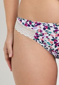 Bas de bikini floral avec des motifs de feuilles violettes et roses. Présente une dentelle le long de la taille et un accent en bouton unique.