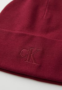 Burgundy beanie made from soft knit fabric, featuring a folded cuff with embroidered "cK" logo in matching thread.