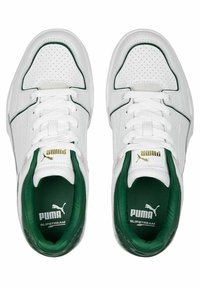 White sneakers with green accents, perforated leather panels, flat white laces, and a padded collar. Features gold logo detail on the tongue.