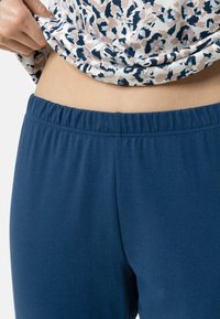 Marina blå byxor med elastisk midja, tillverkade av mjukt tyg, med en slät textur och en figurnära design, som matchas med en mönstrad topp.