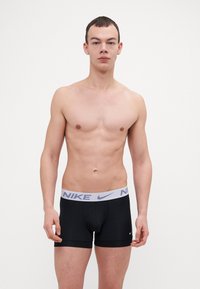 Crne bokserice s bijelim elastičnim pojasom na kojem se nalazi Nike logo. Glatka tekstura tkanine, uski fit i dužina do sredine bedra.