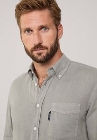 Camicia button-up grigio chiaro realizzata in tessuto testurizzato; presenta una tasca sul petto con un piccolo tag. Collo classico e bottoni bianchi.