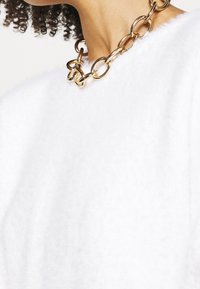 Weißer, flauschiger Textiltop mit Rundhalsausschnitt, ergänzt durch eine klobige Goldkette mit großen Gliedern.