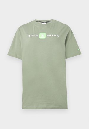 Βαμβακερό κοντομάνικο μπλουζάκι σε ανοιχτό πράσινο χρώμα, με το λογότυπο "NIKE SHOX" σε λευκό και πράσινο στο μπροστινό μέρος και ένα μικρό σήμα Nike στον κοντό μανίκι.