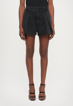 Black pleated shorts with a high waist design, made of denim fabric. Paired with strappy black heels, showcasing a streamlined silhouette.