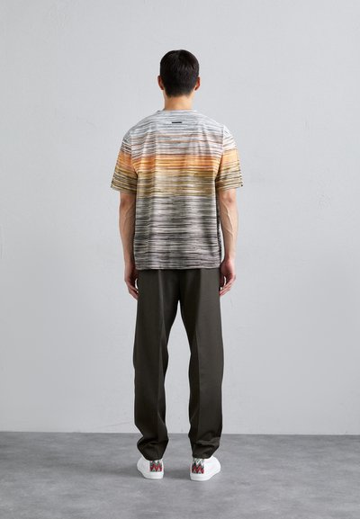 Short-sleeve shirt in a gradient of gray, orange, and yellow stripes, paired with dark trousers and white sneakers featuring patterned accents.