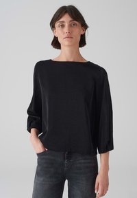 Schwarzes, locker sitzendes Oberteil mit quadratischem Ausschnitt und Dreiviertelärmeln, aus einem weichen, strukturierten Stoff, kombiniert mit dunkler Denim.