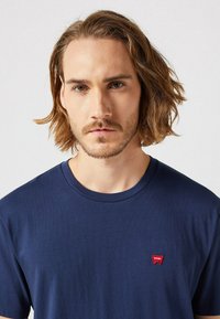 Marineblauwe katoenen t-shirt met een ronde hals, korte mouwen en een klein rood geborduurd logo op de linkerkant van de borst. Glad textuur.