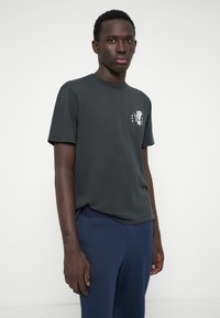 Tamsiai pilka medvilninė marškinėliai su priekinio plano grafika, kuriame pavaizduotas dizainas ir žvaigždės. Apvalus iškirpimas, trumpomis rankovėmis, laisvas siuvimas.