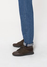 Brązowe buty z mieszanki skóry i zamszu, z okrągłym noskiem i sznurowanym zapięciem, w zestawieniu z podwiniętymi niebieskimi dżinsami.