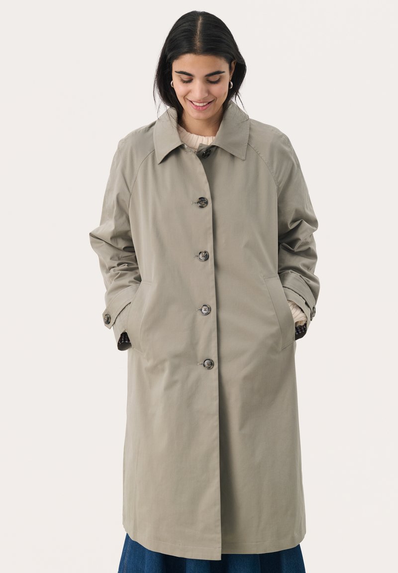 Khaki trench coat s designem na jedno ředění, velkým límcem a knoflíkovým zapínáním. Obsahuje boční kapsy a ohrnovací rukávy. Hladká textura.