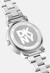 Montre en acier inoxydable avec finition polie, dotée d'un boîtier rond et d'un bracelet argenté, marquée "DKNY" au dos, étanche jusqu'à 5 ATM.
