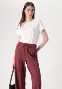 White short-sleeve t-shirt paired with burgundy drawstring pants featuring side seams and a relaxed fit. Model holds a black handbag.