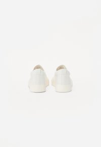 Hvite lerretsko med en teksturert overflate, rund tå og gummisåler. Minimalistisk design med tonale sømmer og lavprofil.