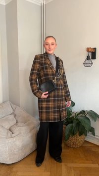 Geruite blazer in bruin- en geeltinten met een zwarte leren crossbodytas. Zwarte wijde broekspijpen en een grijze top maken de outfit compleet.