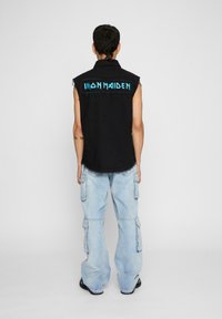 Fekete ujjatlan mellény, amelyen hátul "IRON MAIDEN" felirat található kék betűkkel. Világoskék, bő szárú cargo nadrággal viselve, oldalsó zsebekkel.