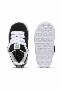 Baskets en suède noir avec des lacets blancs et des semelles en caoutchouc. Présentent une étiquette de logo verte, des accents dorés à l'intérieur et une semelle extérieure texturée blanche.