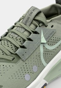 Groene sportieve schoenen met een gestructureerde bovenkant, perforaties voor ademend vermogen, een opvallende patroonoverlay en een gevoerde zool.
