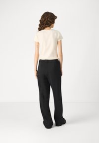 Short-sleeve cream t-shirt paired with black, loose-fit trousers. T-shirt has a round neckline; trousers have belt loops and a straight leg design.