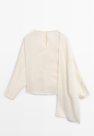 Cremefarvet bluse med lange ærmer og asymmetrisk draperet stofdetalje på det ene ærme samt en lille knaplukning bagpå.