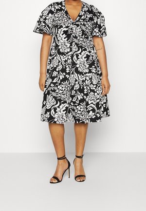 Schwarz-weißes Blumenkleid mit kurzen, gepufften Ärmeln und V-Ausschnitt. Das Kleid hat eine taillierte Taille und weitet sich knielang.