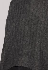 Pull gris en maille avec texture côtelée verticale et coupe ample. Le tissu semble doux, avec un ourlet brut en bas.