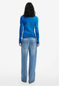Blaues Langarmoberteil mit floralem Muster, kombiniert mit hellblauen weit geschnittenen Jeans mit mittelhohem Bund und Hintertaschen.