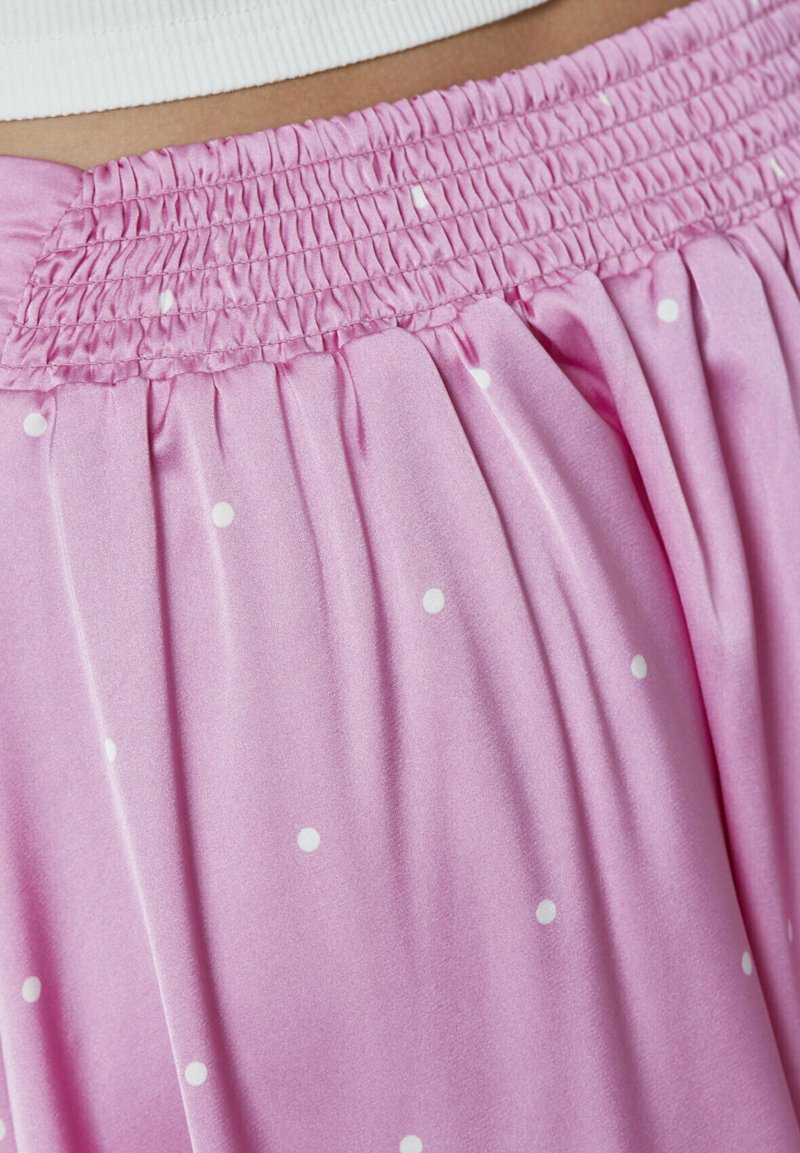 Rosa satin nederdel med hvide polkaprikker, med en smocket talje og blødt, flydende stof drapering.