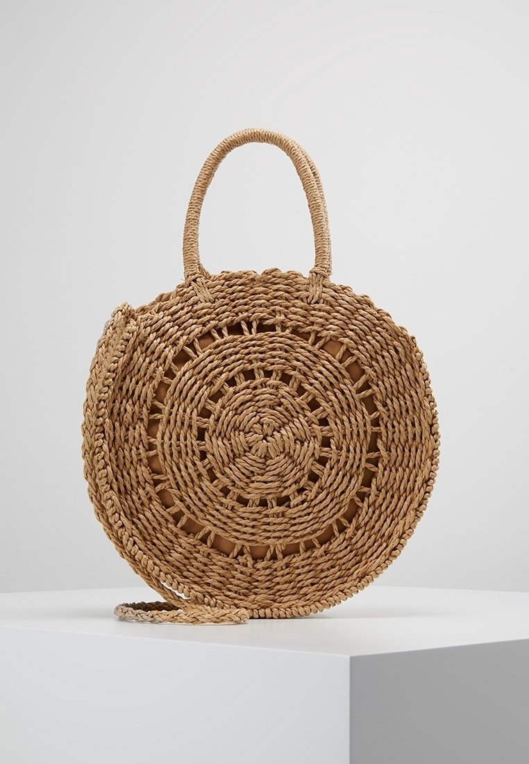 Sac à main rond en paille tressée avec poignée supérieure et bandoulière, présentant un motif circulaire tressé de couleur naturelle.