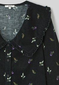 Blouse en velours côtelé noir avec imprimé floral comprenant des accents blancs, violets et verts. Elle possède un col froncé et une fermeture à boutons sur le devant.