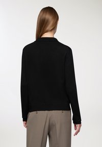 Czarny sweter dziany z kołnierzykiem, długimi rękawami i prążkowanym wykończeniem. Gładka faktura, dopasowany fason, noszony na beżowych spodniach z podwójnymi guzikami.