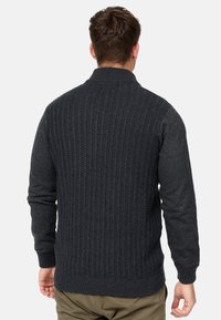 Mørkegrå sweater med en struktureret ribstrik på ryggen og glatte ærmer, med høj krave og tætsiddende manchetter.