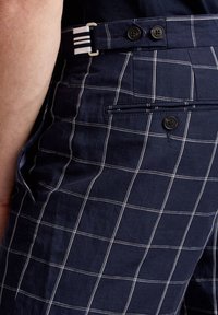 Námořnické kárované kalhoty vyrobené z lehkého materiálu s bílou mřížkou, vybavené dvěma černými knoflíky a proužkovaným poutkem na opasek.