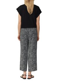 Zwarte top met korte mouwen gecombineerd met loszittende zwarte en witte broek met geometrisch patroon. Bevat platte sandalen.