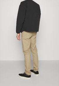 Černá prošívaná bunda, béžové slim-fit kalhoty a černé tenisky s bílými podrážkami. Texturovaná tkanina a jednoduchý design bez viditelných vzorů.