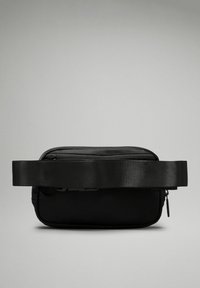Sac bandoulière noir avec un extérieur en nylon texturé, fermeture éclair sur le dessus et sangle réglable. Forme rectangulaire au design minimaliste.