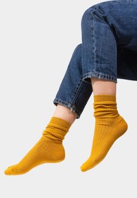Żółte skarpetki z prążkowanej tkaniny, wykonane z miękkiego materiału, z bezpiecznym ściągaczem i luźnym krojem. Projekt zawiera pionowe prążki dla dodania faktury.