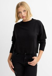 Suéter negro, recortado, en un tejido de punto texturizado con un cuello redondo y hombros caídos, que presenta puños y dobladillo acanalados.