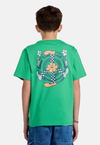 Groene katoenen T-shirt met een gekleurde grafische print op de achterkant, met bloem- elementen en geblokte patronen op een cirkelvormig motief.