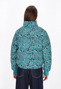 Jachetă căptușită de culoare turcoaz, cu un print de leopard negru și roz. Guler înalt și manșete ribbate pentru un plus de căldură.