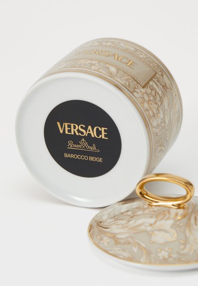 Balta porcelāna burka ar smalku bēša un zelta Barokko rakstu, uz vāka ar zelta riņķa rokturi un melnu etiķeti ar uzrakstu "VERSACE".