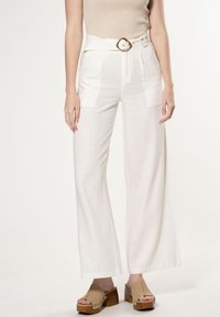 Witte linnen wijde broek met een gladde textuur en geplooide details aan de voorkant, gecombineerd met een tan platform sandaal. Gouden riemaccent.
