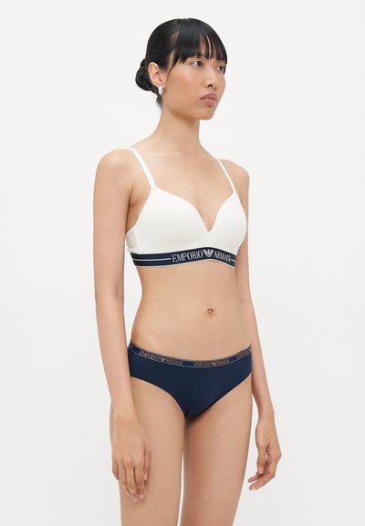 White bra with a deep V-neck and navy band labeled "Emporio Armani"; matching navy bikini bottom with a contrasting waistband.