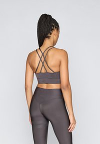 Sutiã desportivo cinzento com alças cruzadas e textura suave. Combinado com leggings de cintura alta com riscas subtis perto da bainha.