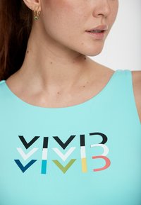 Débardeur aqua présentant un design graphique audacieux en noir, blanc, bleu-vert, vert, jaune et corail. Tissu lisse et ajusté avec un col rond.