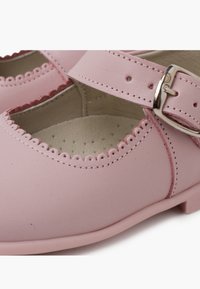 Zapatos de cuero rosa con un diseño de borde con volutas, una tira estrecha con una hebilla de plata y una superficie interior lisa con perforaciones.