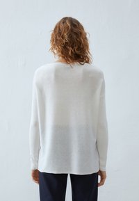 Kevyt valkoinen neule paitaminen, joka on rento ja jossa on ribbireunat sekä takasaumadetaili. Pehmeä, hieman läpikuultava kangas. Yhdistetty tummiin housuihin.