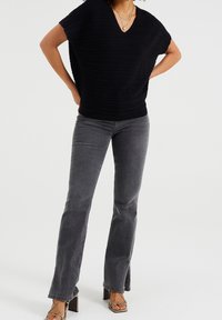 Černý žebrovaný pletený top s výstřihem do V a krátkými rukávy, spárovaný se šedými zvonovými džíny se bočními štěrbiny na lemu. Masivní sandály na podpatku.