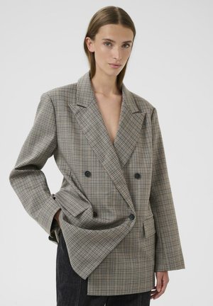 Dobbeltradet blazer i gråt og beige ternet mønster med store hakknappede revers, forlommer og sorte knapper.